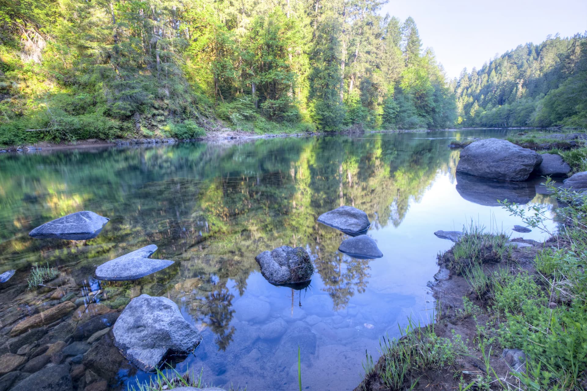 A calm stretch of the North Umpqua River reflecting the forest, with boulders in clear water